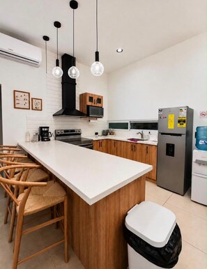Una cocina moderna con una isla central, armarios de madera, microondas integrado y un refrigerador de acero inoxidable.