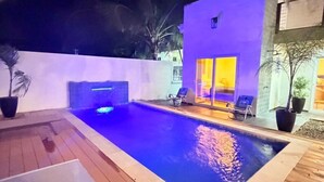 A swimming pool with a wooden deck, a lounge chair, and a modern building in the background.