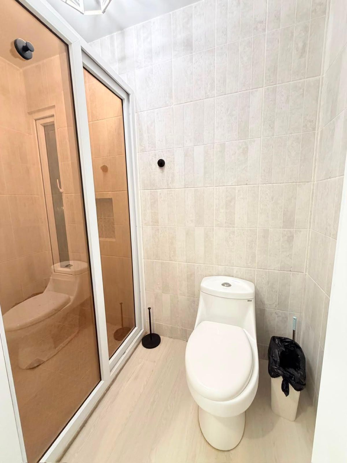 Ein Badezimmer mit Toilette, Duschkabine und Mülleimer.