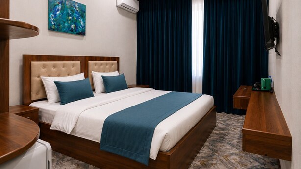 Quarto de hotel com cama, televisão de tela plana, pintura na parede e janela com cortinas.