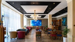 Um lobby de hotel com design moderno, apresentando uma grande tela, assentos confortáveis e um lustre.