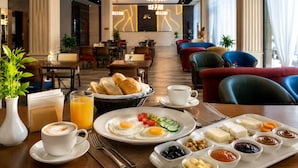 Uma mesa de café da manhã com uma bandeja de ovos, torradas e diversas geleias, uma xícara de café e um copo de suco.