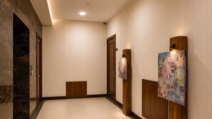 Um corredor com parede de mármore, portas de madeira e chão ladrilhado.