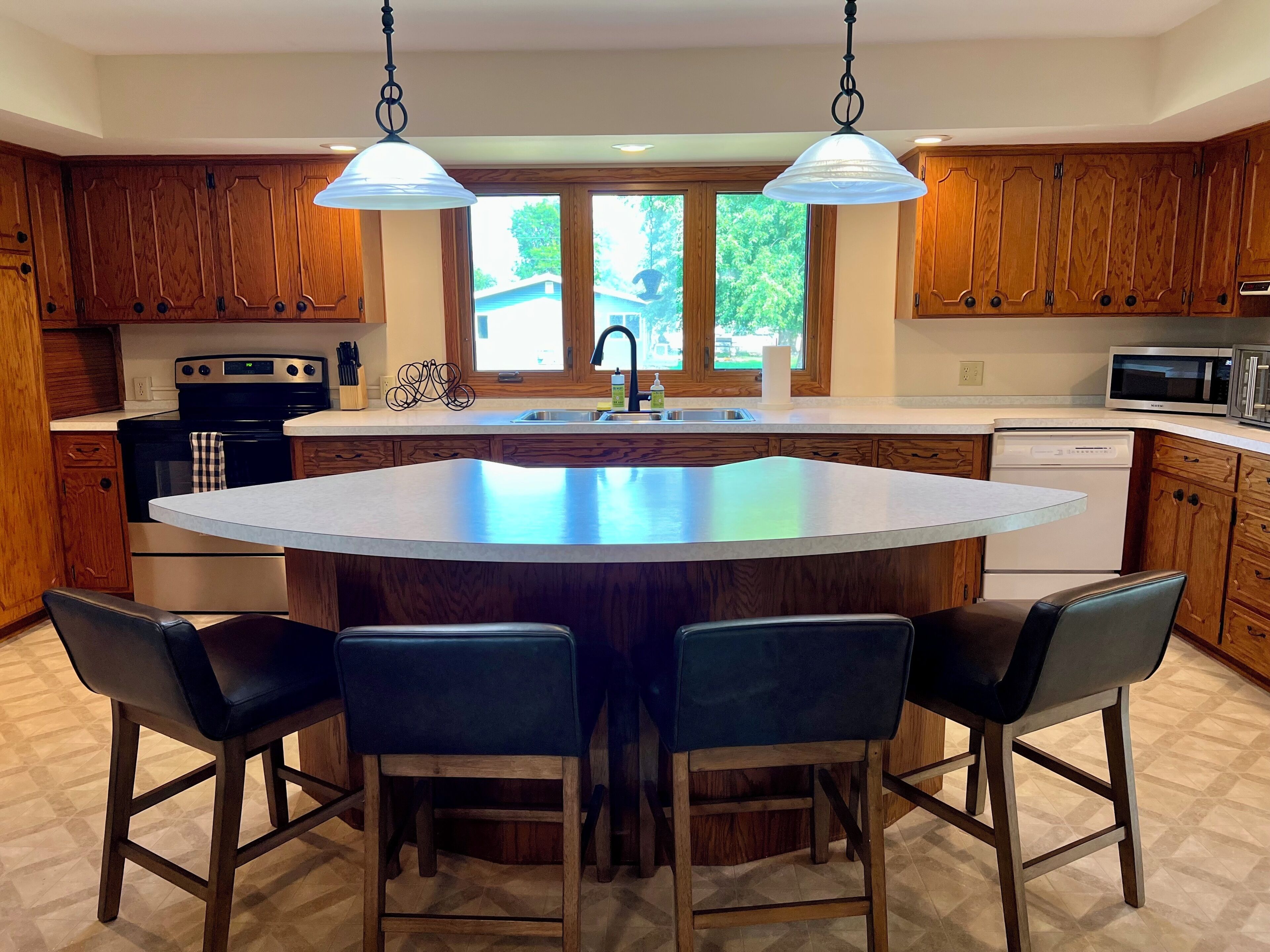 A kitchen with a central island, wooden cabinets, a stainless steel oven, and a microwave.