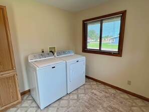 A laundry room with two white front-loading washers and dryers, a wooden cabinet, and a window with blinds.