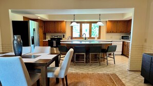 A modern kitchen with a central island, wooden cabinets, and a dining area with a rug. - Spacious Independence Home - Conveniently Located (Independence)