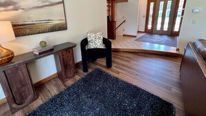 A living room with a wooden floor, a black armchair, a coffee table, a lamp, a bookshelf, and a painting on the wall. - Spacious Independence Home - Conveniently Located (Independence)