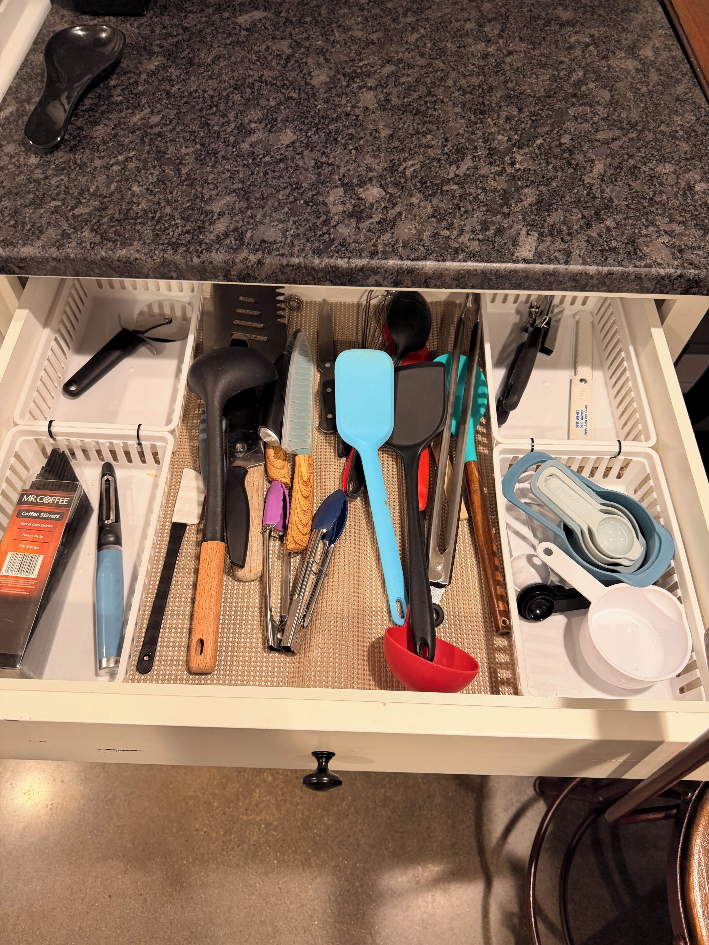 A drawer with kitchen utensils and a coffee maker.