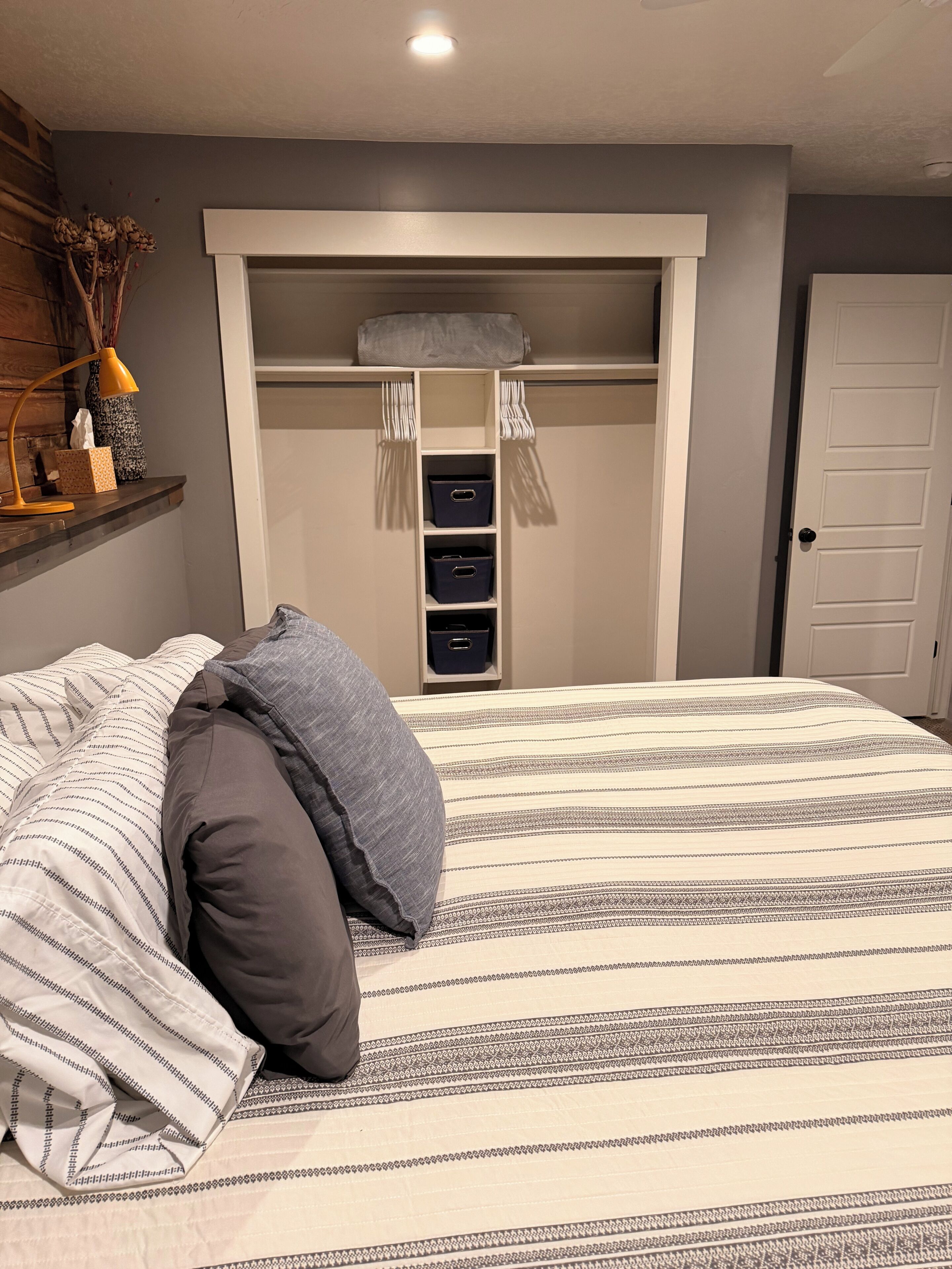 A bedroom with a bed, a wardrobe with storage boxes, and a bedside table with a lamp.