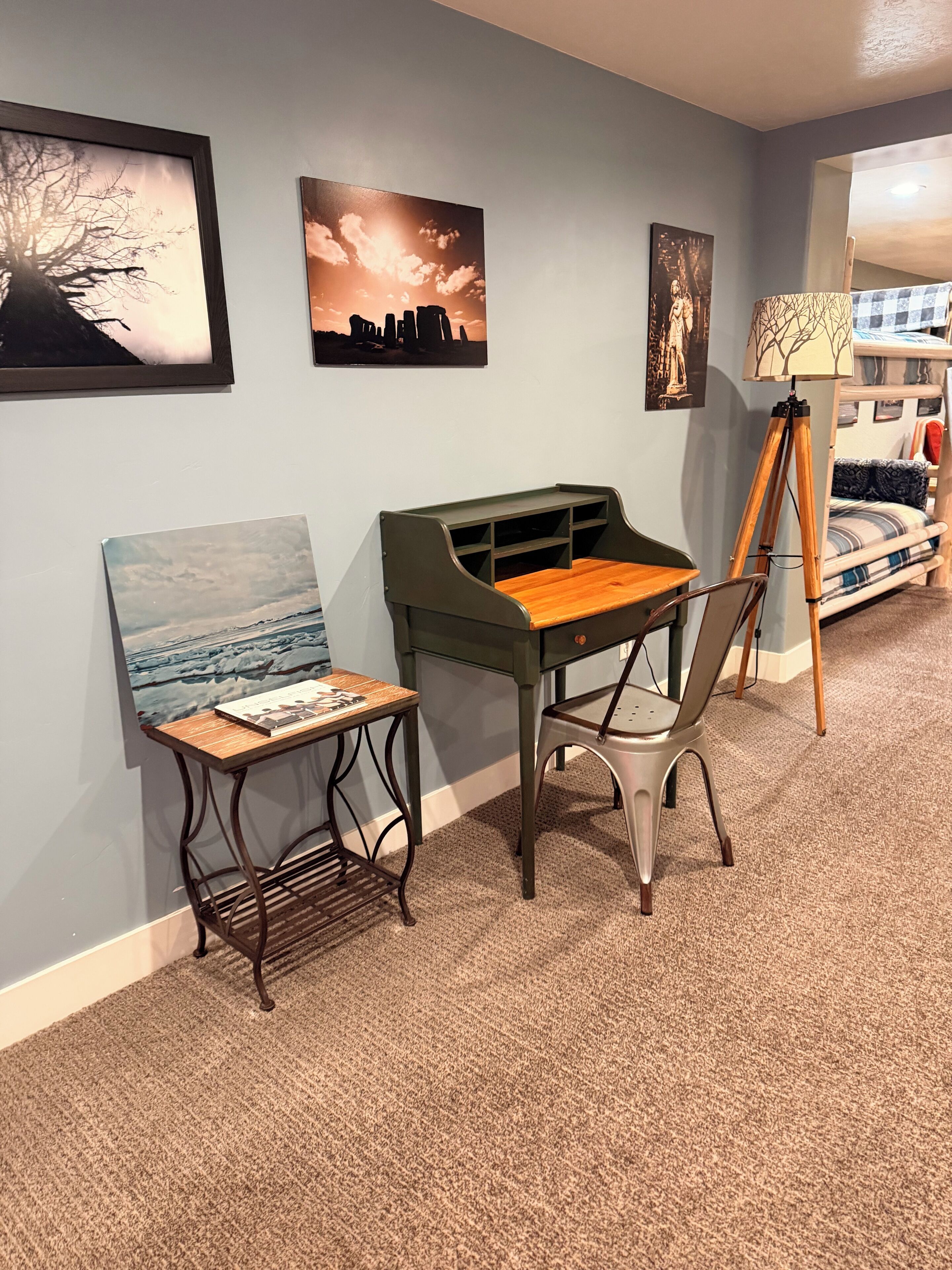 A room with a green desk, a chair, a lamp, and artwork on the walls.