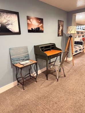 A room with a green desk, a chair, a lamp, and artwork on the walls.
