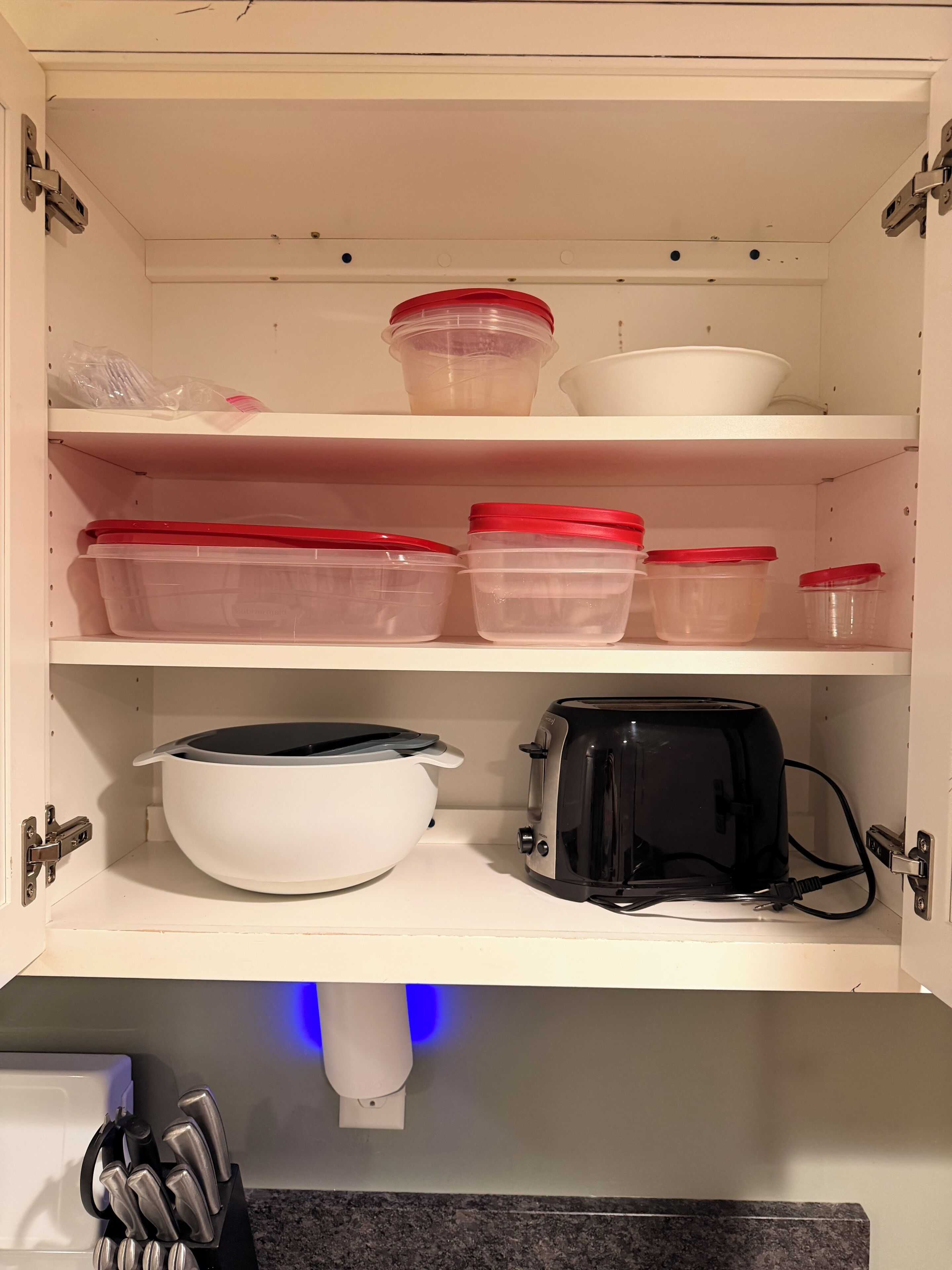 A kitchen cabinet with storage containers, a white pot, and a toaster.