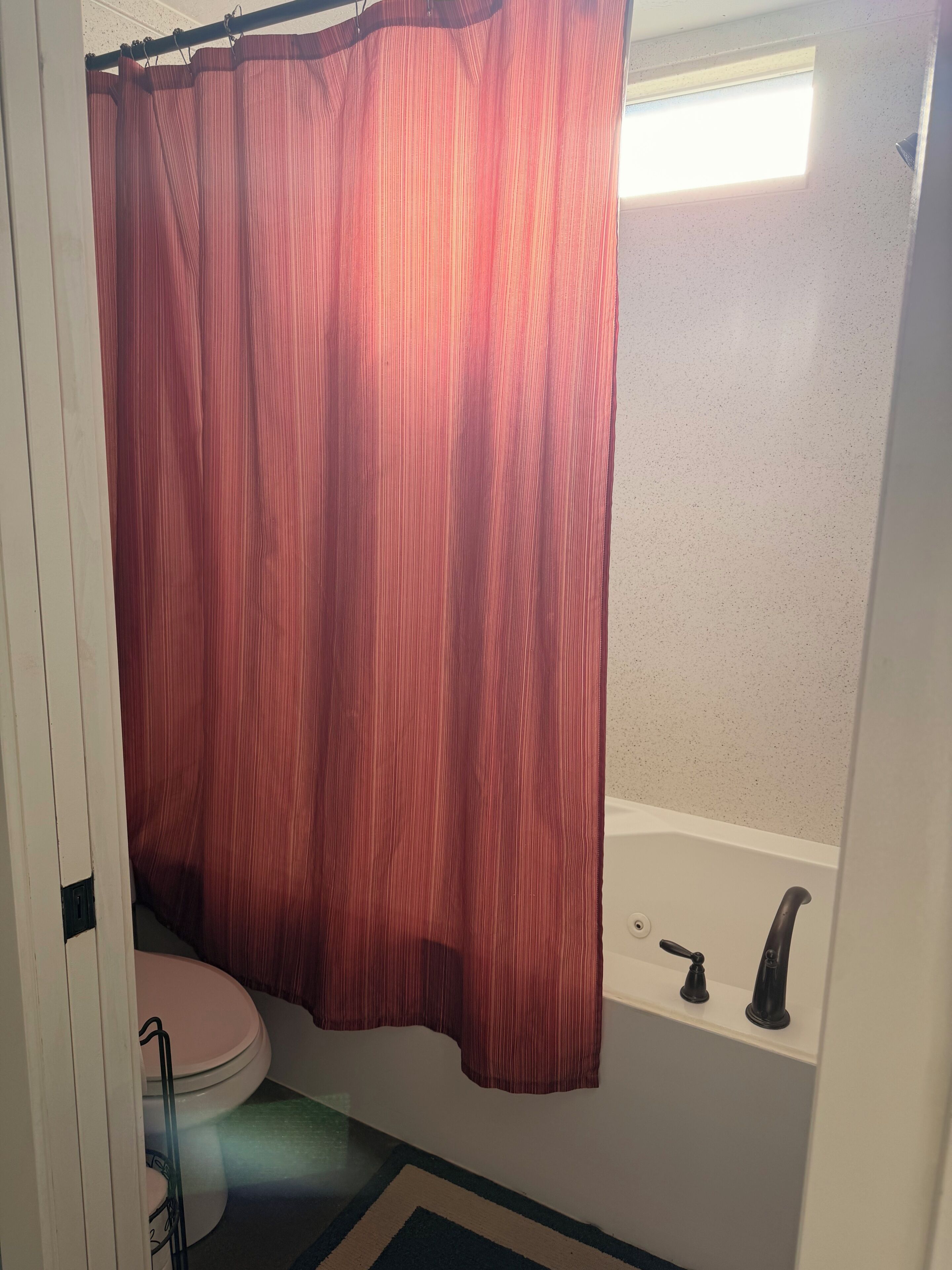 A bathroom with a white bathtub, a pink toilet, and a shower curtain.