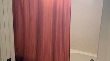 A bathroom with a white bathtub, a pink toilet, and a shower curtain.