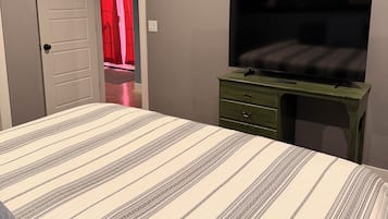 A bedroom with a bed, a desk, a television, and a ceiling fan.