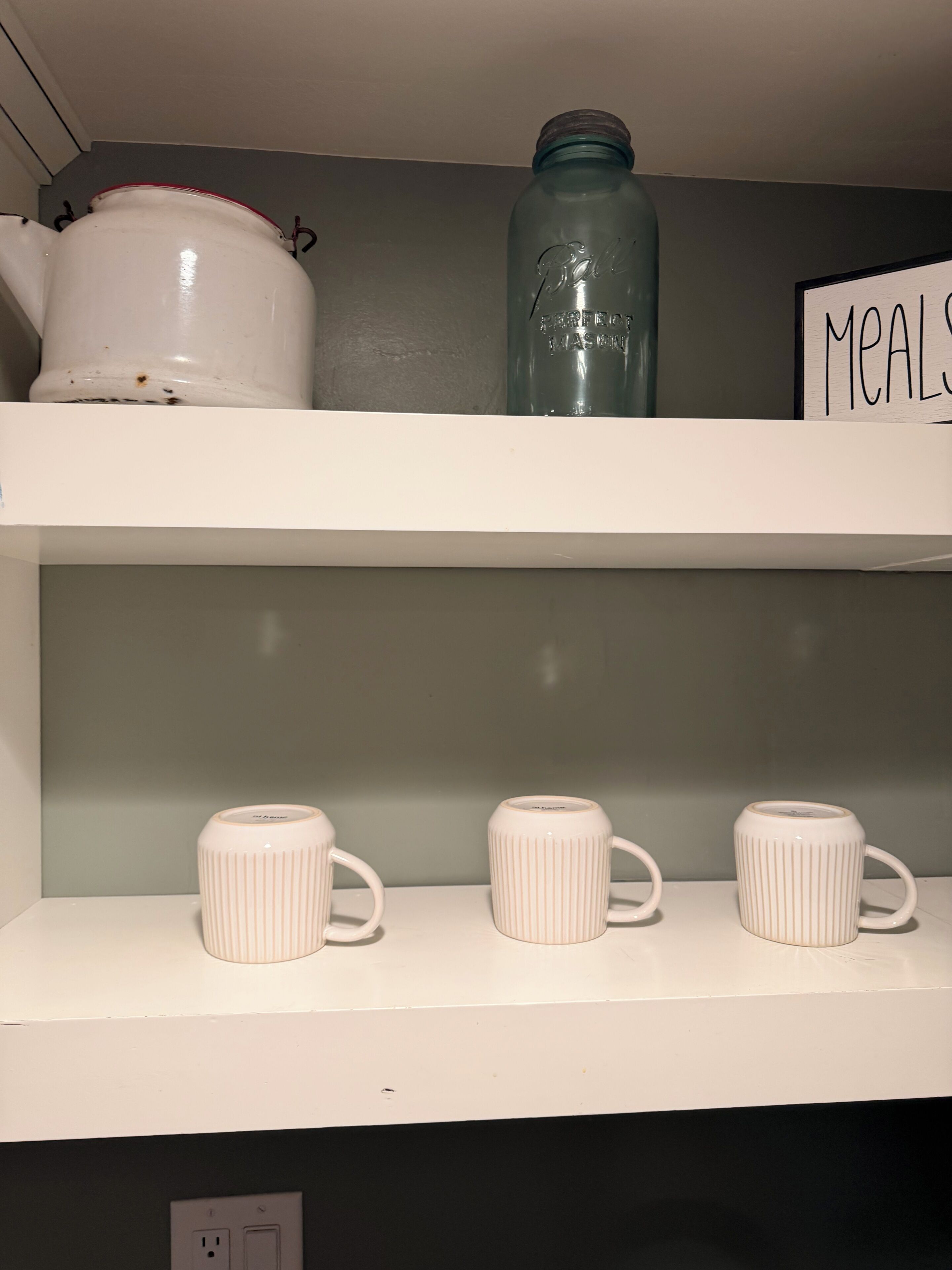 En hylla med en vit kruka, en glasburk och tre muggar med räfflad yta.
