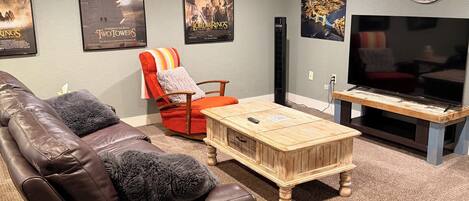 A living room with a brown leather couch, a red armchair, a wooden coffee table, a TV, and movie posters on the wall.