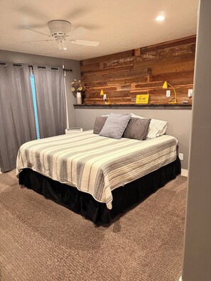 A bedroom with a bed, curtains, a ceiling fan, a wooden wall panel, and a bedside table with lamps. - Quiet 2 Bedroom 1 Bath in Payson, UT (Payson)