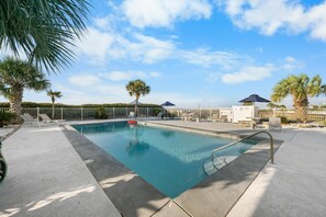 A swimming pool with lounge chairs and umbrellas, surrounded by palm trees and a fence. - GS Plantation East 2109 (Gulf Shores)