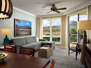 Ein Hotelzimmer mit einer Couch, einem Esstisch, einem Deckenventilator und einem großen Fenster mit Blick auf Grünflächen.