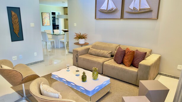 Een moderne woonkamer met een beige bank, een glazen salontafel en een eethoek op de achtergrond.