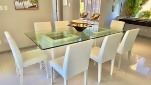 Een moderne eetruimte met een tafel met glazen blad, omringd door witte stoelen.