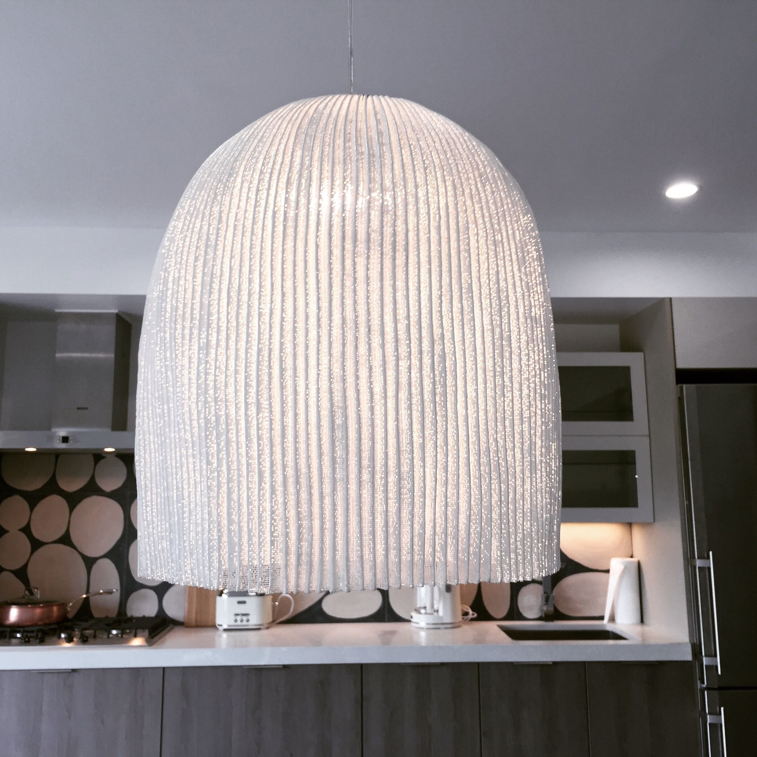 Una cocina moderna con una lámpara colgante de diseño original y listones sobre una encimera.