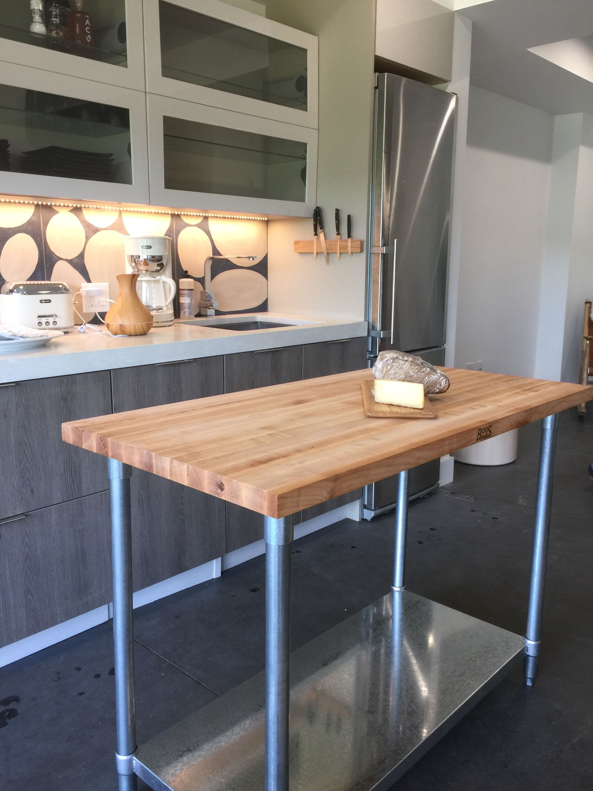 A modern kitchen with a wooden island, stainless steel appliances, and a glass backsplash.