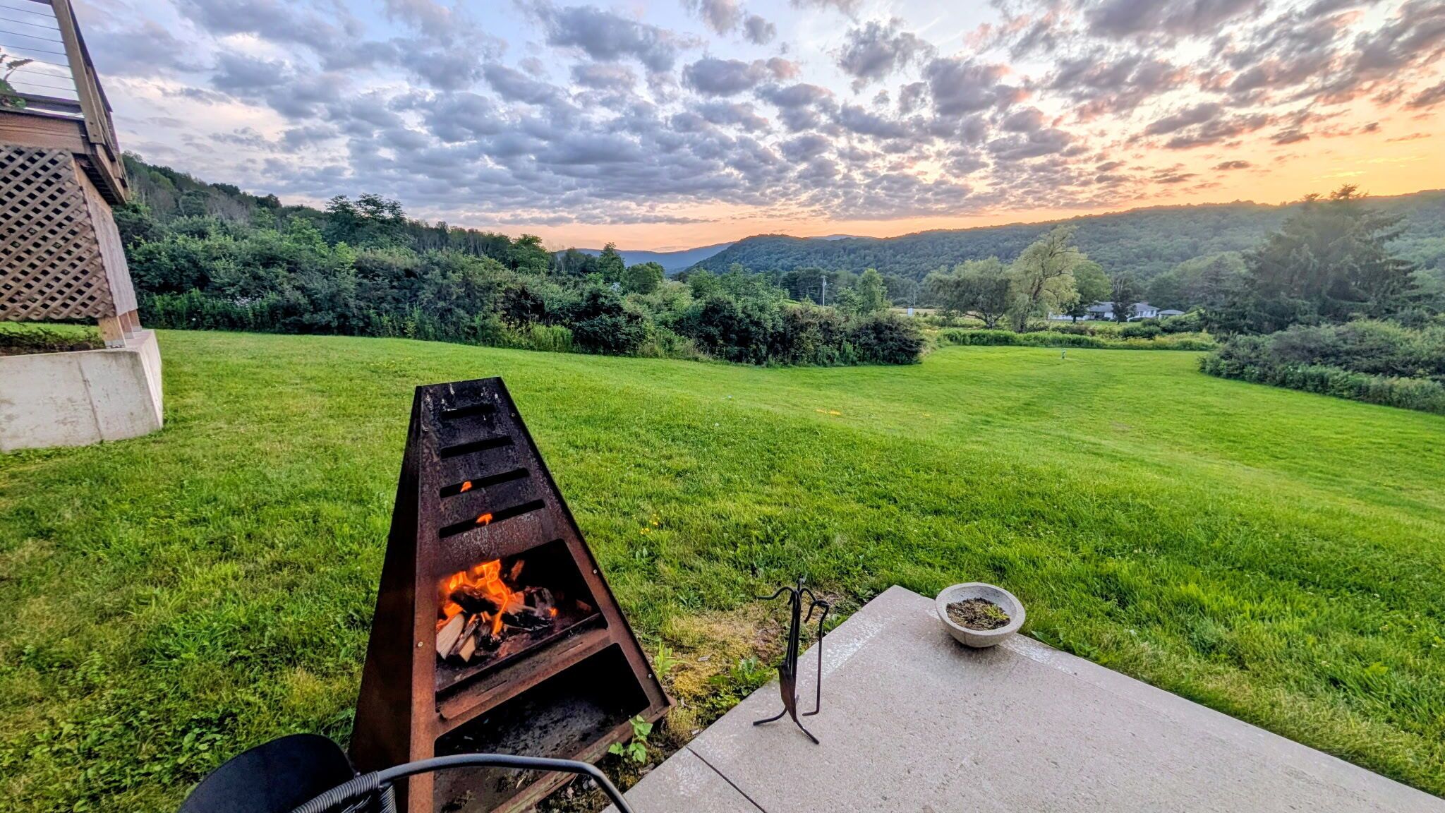 A backyard with a barbecue grill, a concrete table, and a bowl of charcoal.