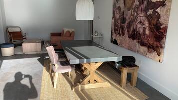 Une pièce avec une longue table, des chaises rembourrées, un luminaire suspendu et un grand tableau accroché au mur.