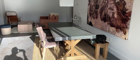 Una habitación con una larga mesa, sillas acolchadas, una lámpara colgante y un cuadro grande en la pared.
