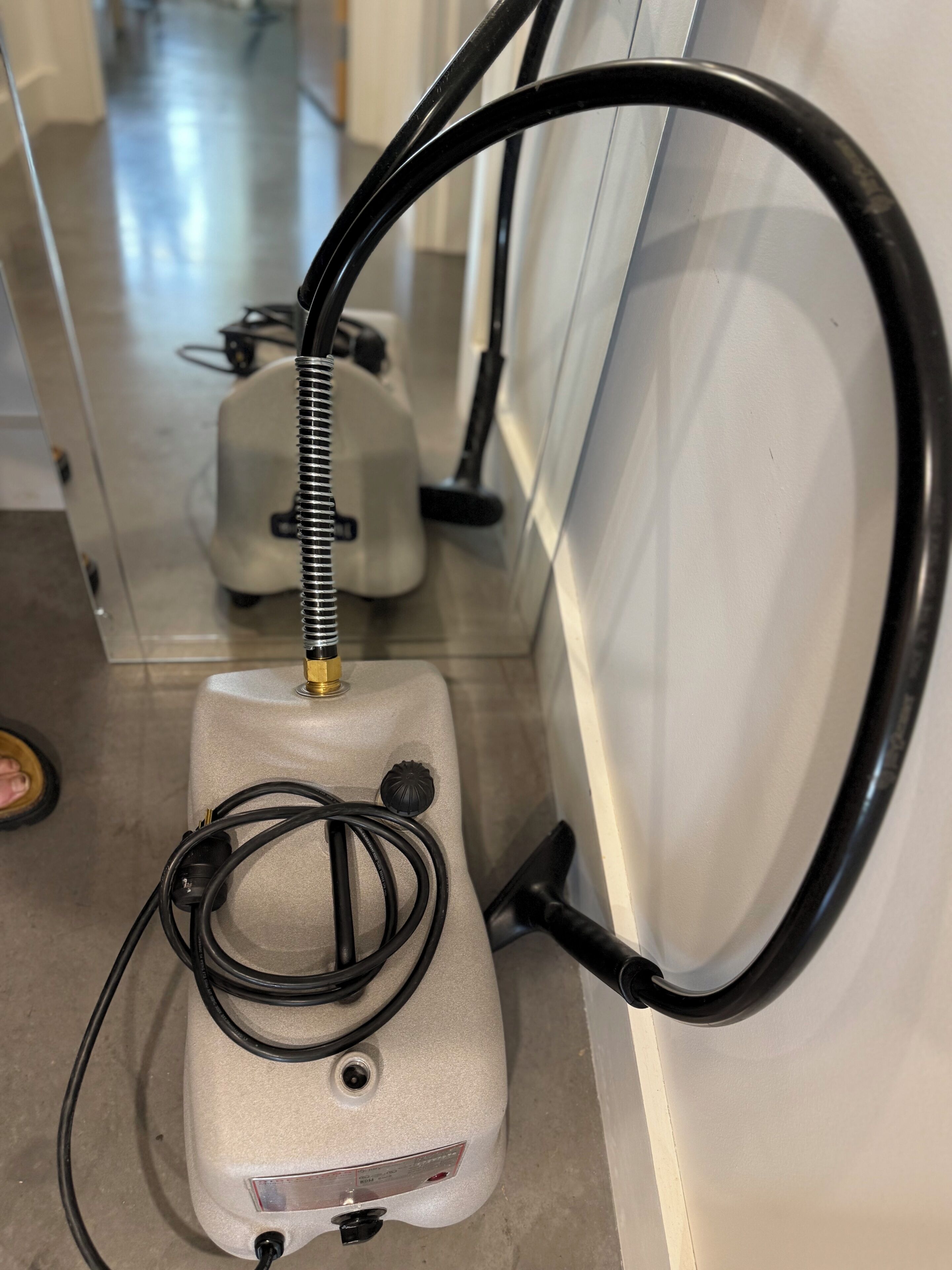 A portable air compressor with a hose and a power cord, placed against a wall.