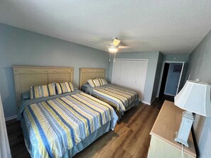 Ein Schlafzimmer mit zwei Betten, einem Deckenventilator, einem Kleiderschrank und einem Schreibtisch mit Lampe.