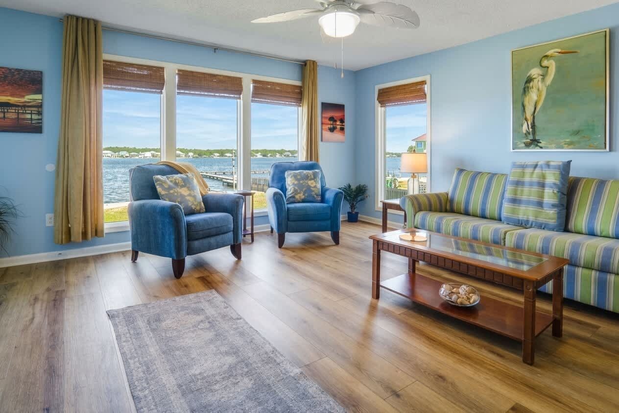 A living room with a view of the water, a blue sofa, two blue armchairs, and a wooden coffee table.