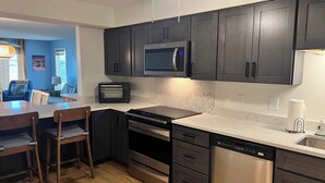 Una cucina moderna con mobili scuri, un forno a microonde, un tostapane, una lavastoviglie e un'area pranzo con tavolo e sedie.