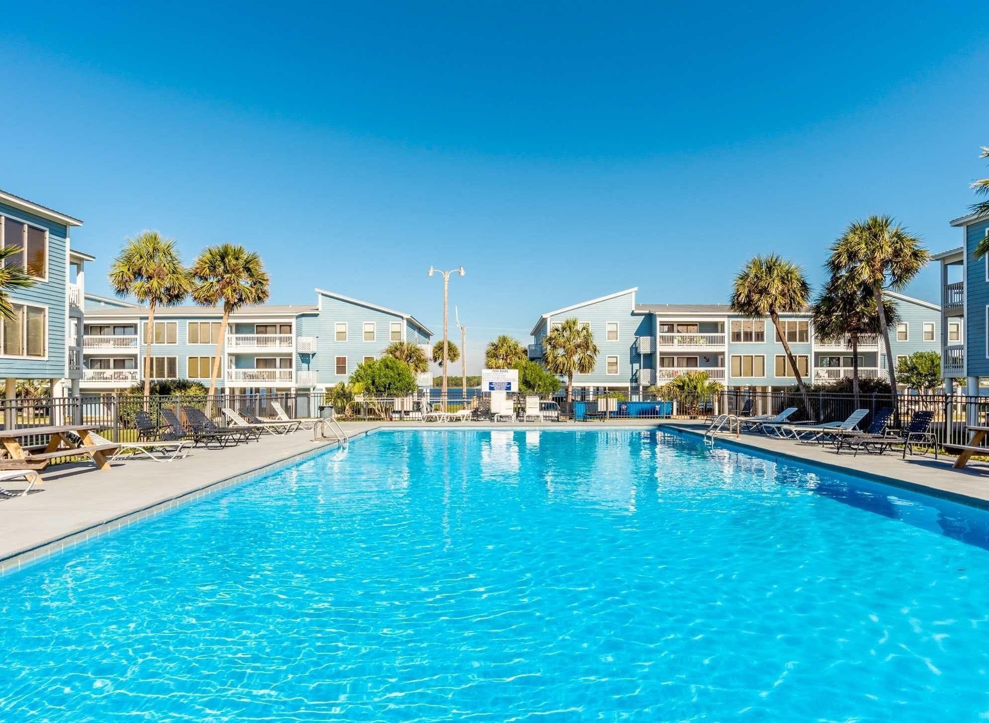 Une piscine entourée de bâtiments à plusieurs étages dotés de balcons, avec des chaises longues et des palmiers.