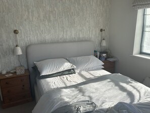 Een slaapkamer met een bed, twee nachtkastjes, een lamp, een raam en een muur met een structuur.