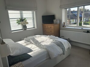 Ein Schlafzimmer mit einem Bett, einem Schminktisch, einem Fernseher, einem Fenster mit Blick auf Häuser und einer Heizung.