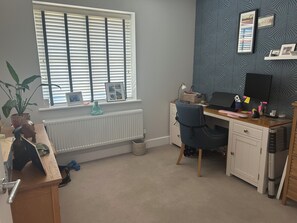 Ein Zimmer mit Schreibtisch, Computer und einem Fenster mit Jalousien.
