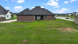 A two-story brick house with a gabled roof, a front porch, and a well-maintained lawn. - Fully Furnished 4-Bedroom Executive Home (Stonewall)