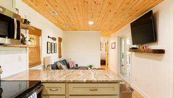 A modern kitchen with a wooden ceiling, built-in appliances, a marble countertop, and a flat-screen TV mounted on the wall.