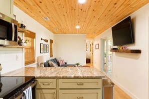 Een moderne keuken met een houten plafond, ingebouwde apparatuur, een marmeren aanrechtblad en een flatscreen televisie aan de wand.