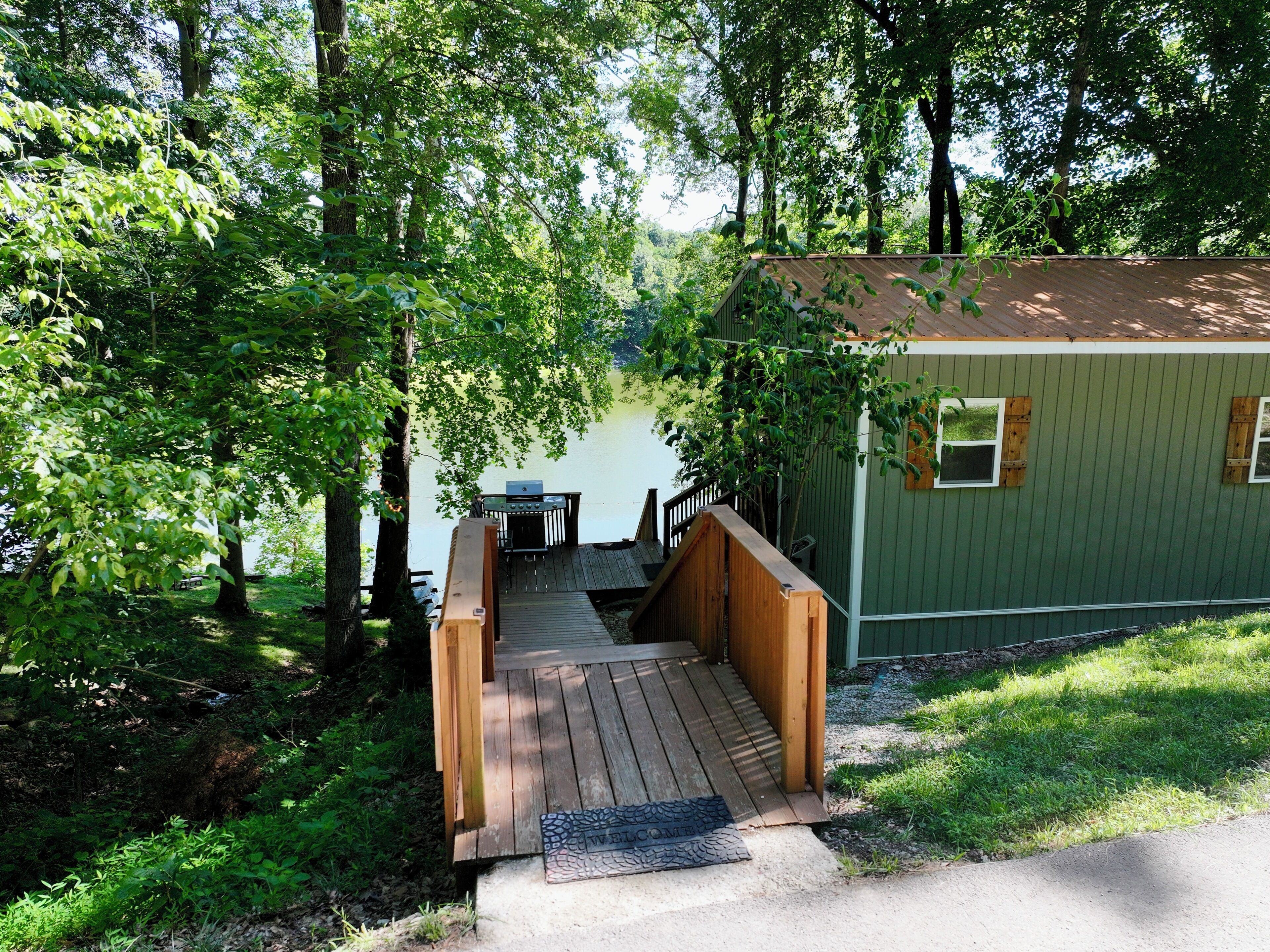 A wooden deck leading to a cabin with a dock extending into a lake, surrounded by dense greenery.