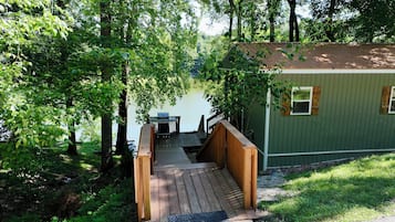 A wooden deck leading to a cabin with a dock extending into a lake, surrounded by dense greenery.