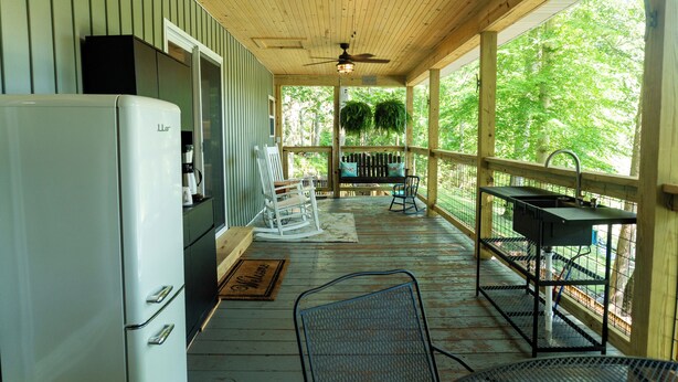 A covered porch with a refrigerator, a rocking chair, and a metal chair.