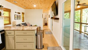 A modern kitchen with a wooden ceiling, a large island, and a sliding glass door leading to an outdoor deck.