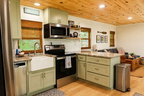 Une cuisine compacte équipée d’un four à micro-ondes, d’une cuisinière et d’un évier. Le plafond est en bois et il y a une fenêtre avec vue.