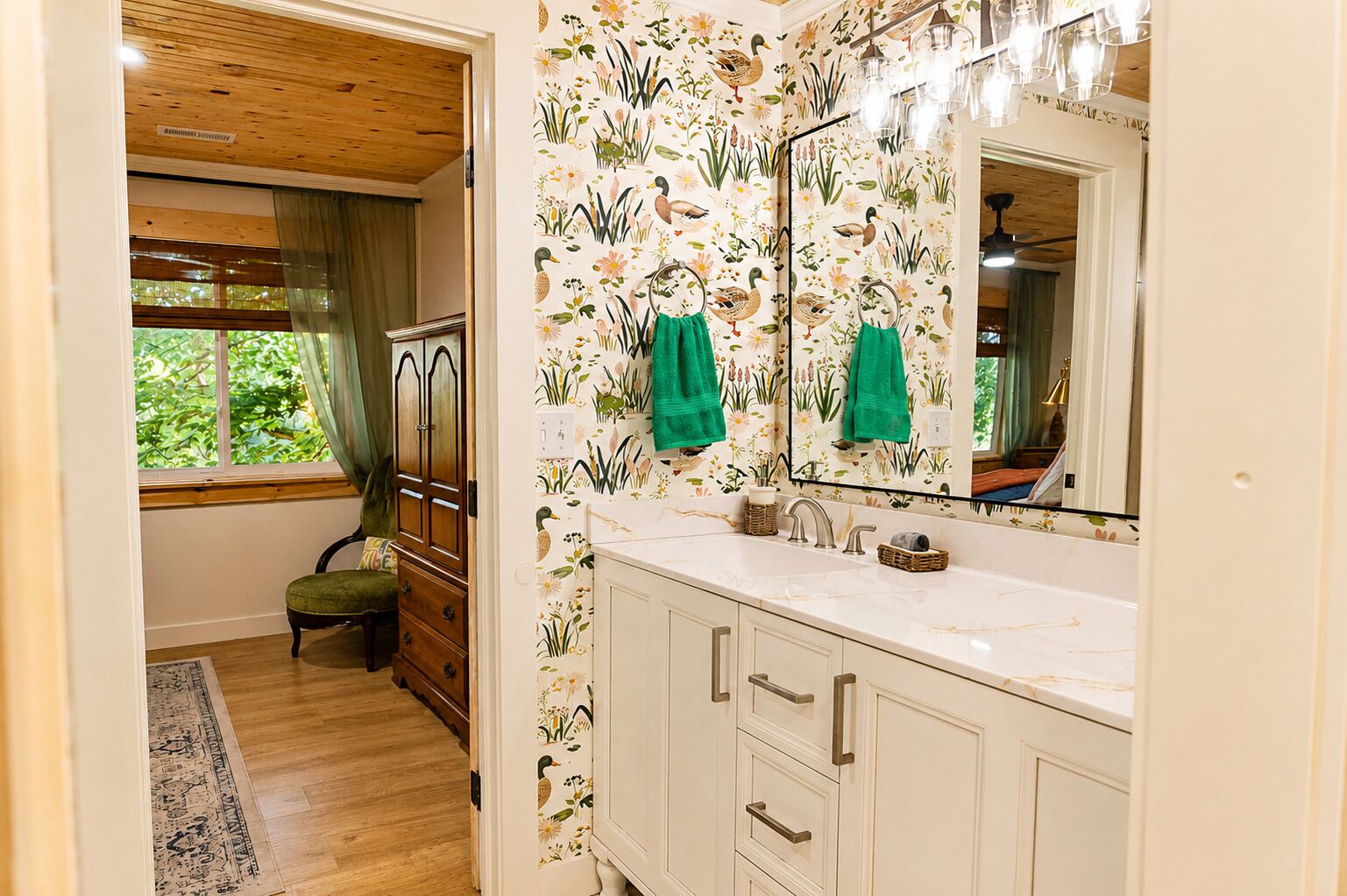 Un bagno con un mobile bagno in legno, uno specchio grande e carta da parati a motivi floreali.