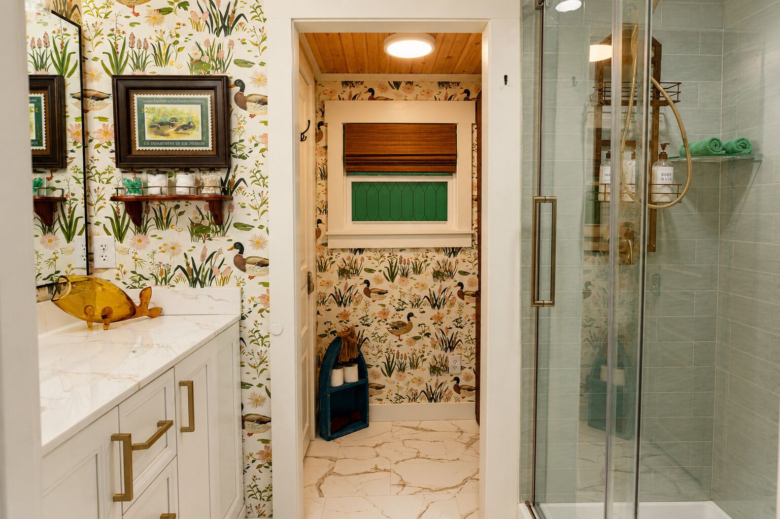 Ein Badezimmer mit Dusche, einem Waschtisch mit Marmorplatte und einer Wand mit Blumenmuster-Tapete.