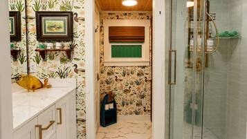 Ein Badezimmer mit Dusche, einem Waschtisch mit Marmorplatte und einer Wand mit Blumenmuster-Tapete.